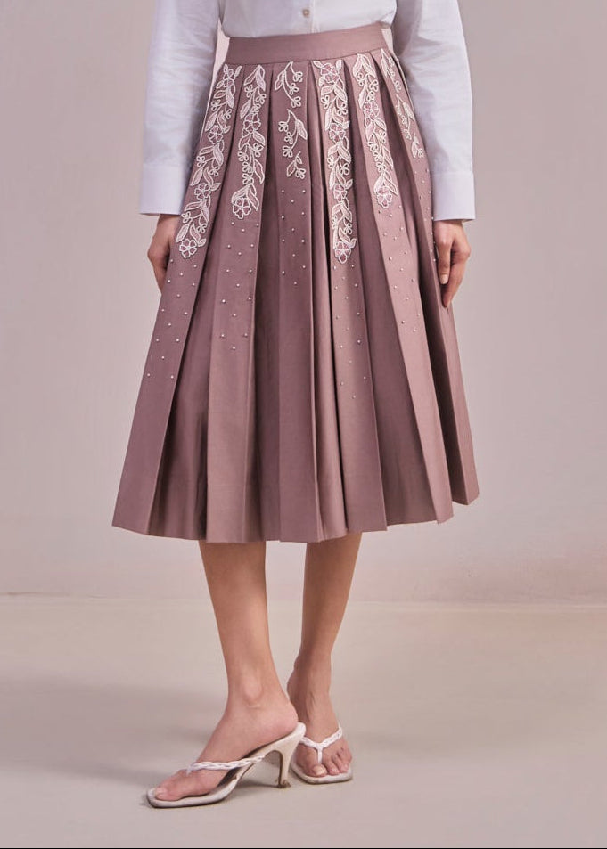 Woman wearing a white blazer and pink skirt with floral embroidery on a plain background