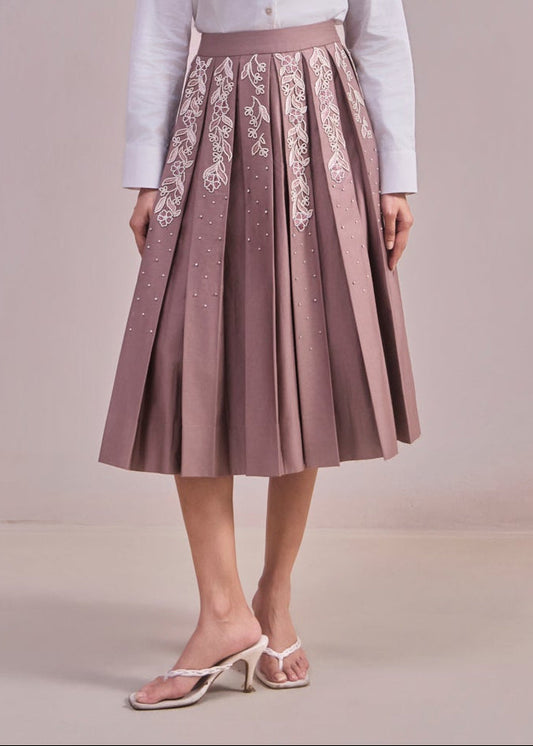 Woman wearing a white blazer and pink skirt with floral embroidery on a plain background