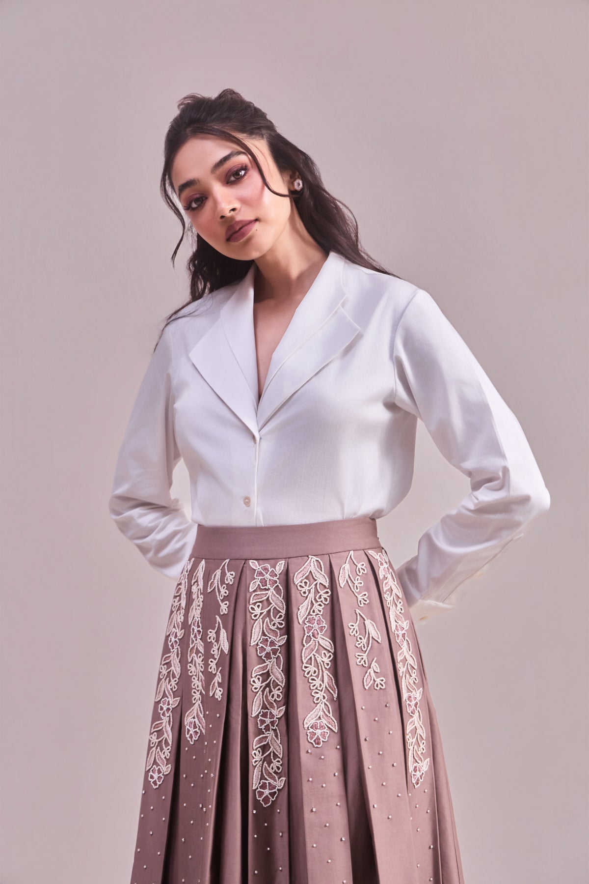 Woman wearing a white blouse and pink skirt with lace details on a plain background