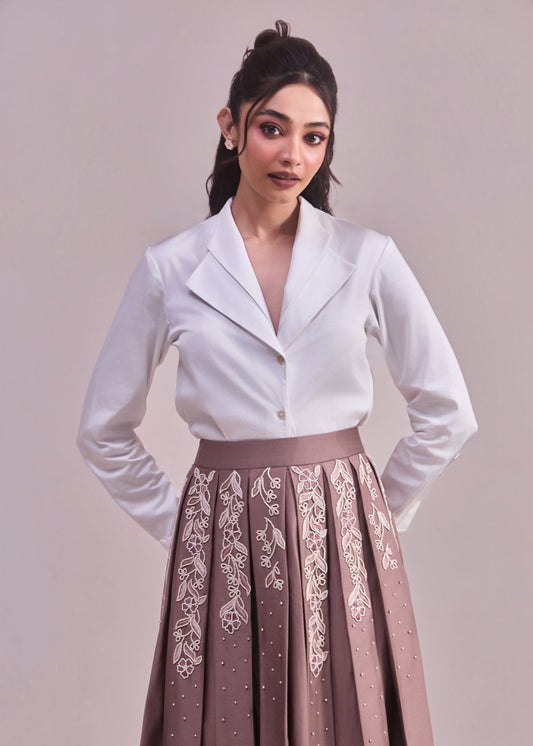 Woman wearing a white top and brown skirt with lace details on a plain background