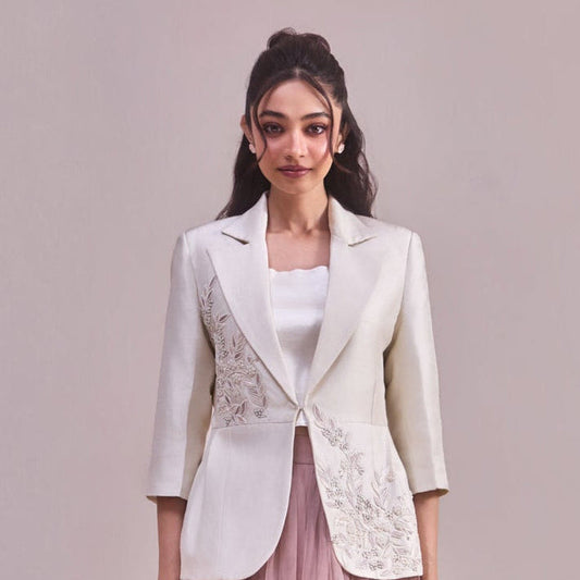 Woman wearing a white blazer with floral embroidery and a pink tulle skirt on a plain background