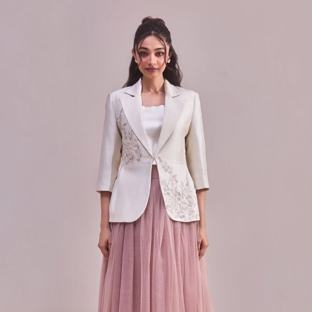 Woman wearing a white blazer with floral embroidery and a pink tulle skirt on a plain background