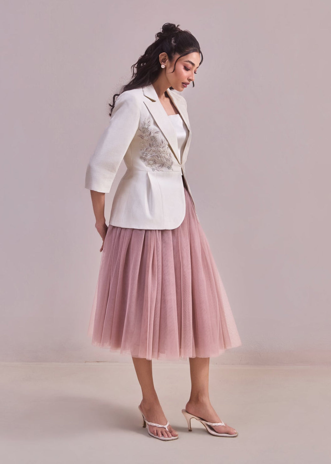 Woman wearing a white blazer and pink tulle skirt on a plain background