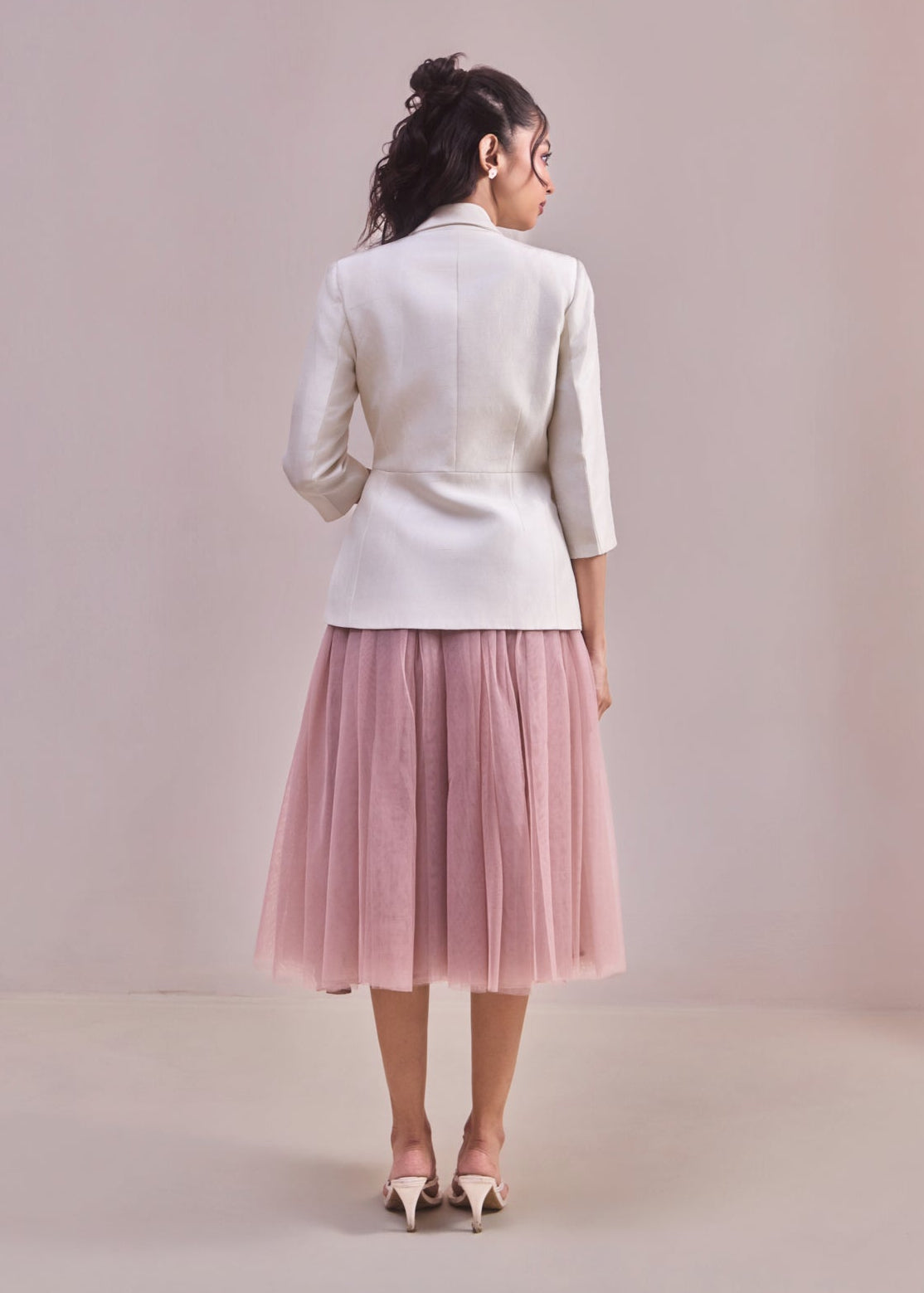 Woman wearing a white blazer and pink tulle skirt on a plain background