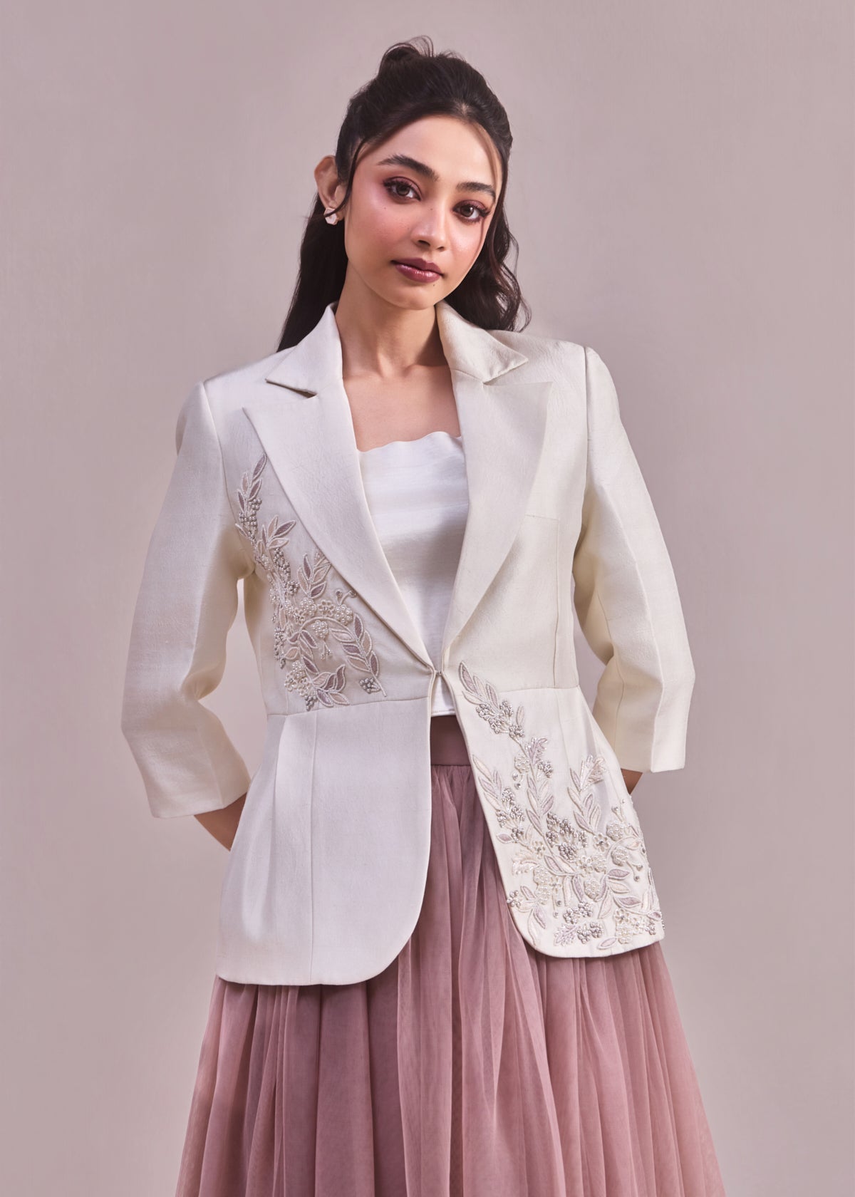 Woman wearing a white embroidered blazer over a pink dress on a plain background
