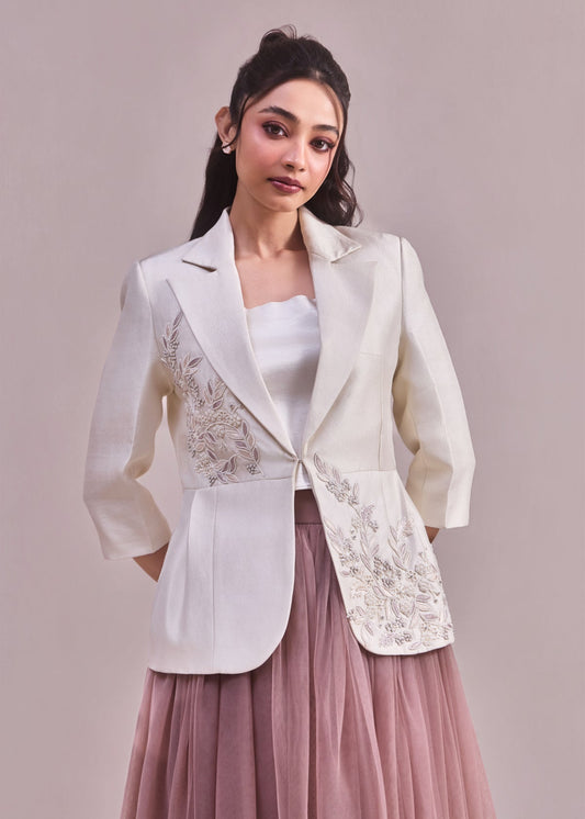 Woman wearing a white embroidered blazer over a pink dress on a plain background