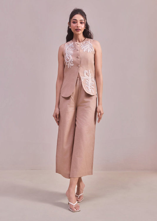 Woman wearing a beige outfit with floral details on a plain background