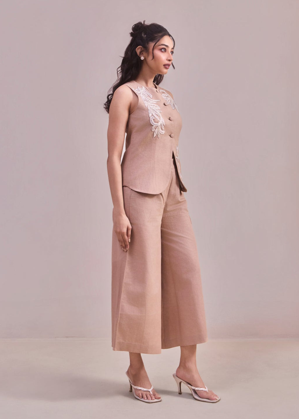 Woman wearing a beige outfit with wide-leg pants against a plain background