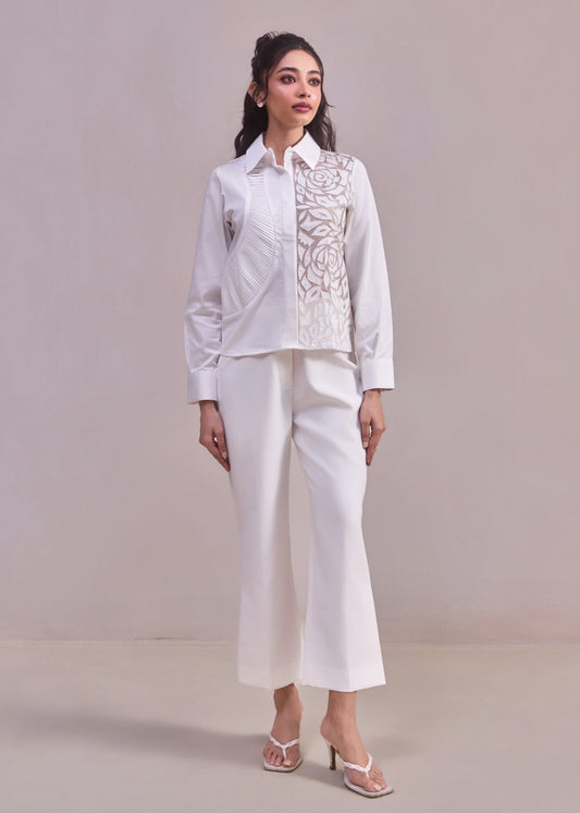 Woman wearing a white embroidered blouse and pants against a plain background