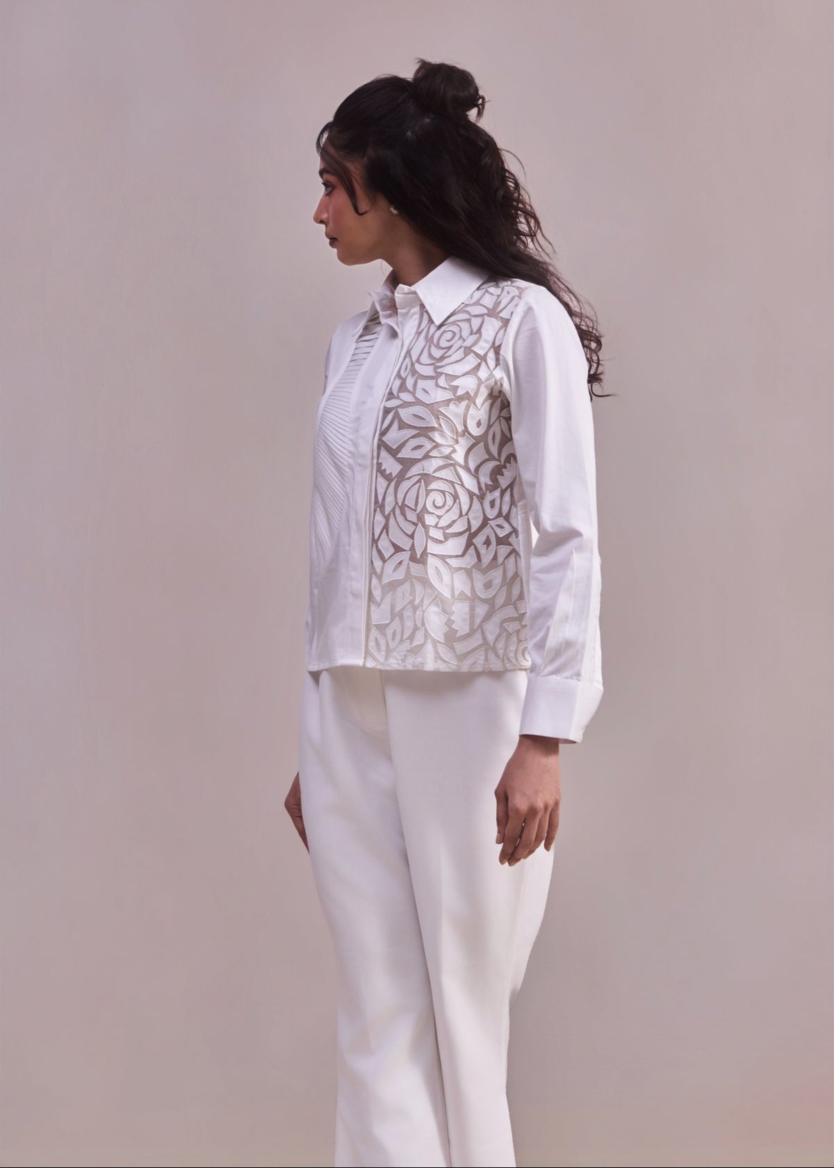 Woman wearing a white blouse with floral embroidery and white pants against a plain background