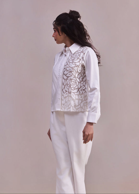 Woman wearing a white blouse with floral embroidery and white pants against a plain background