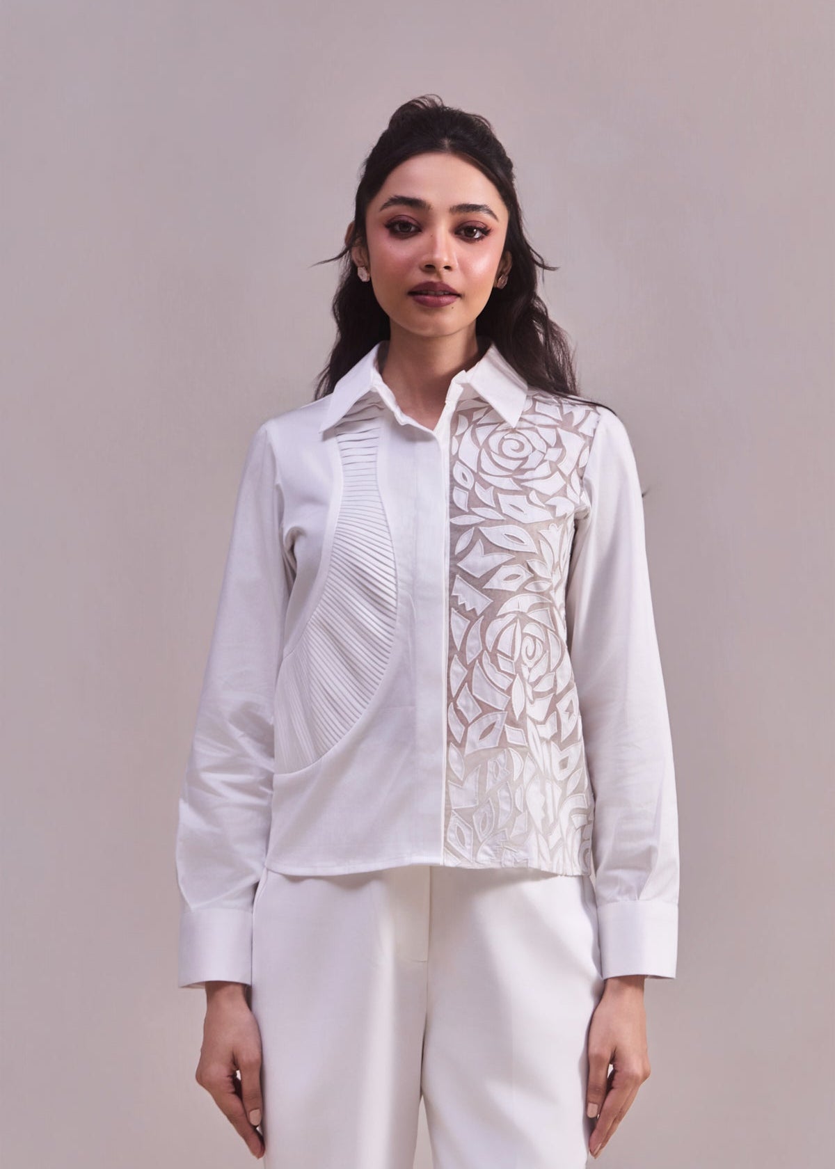 Woman wearing a white blouse with intricate patterns on a plain background