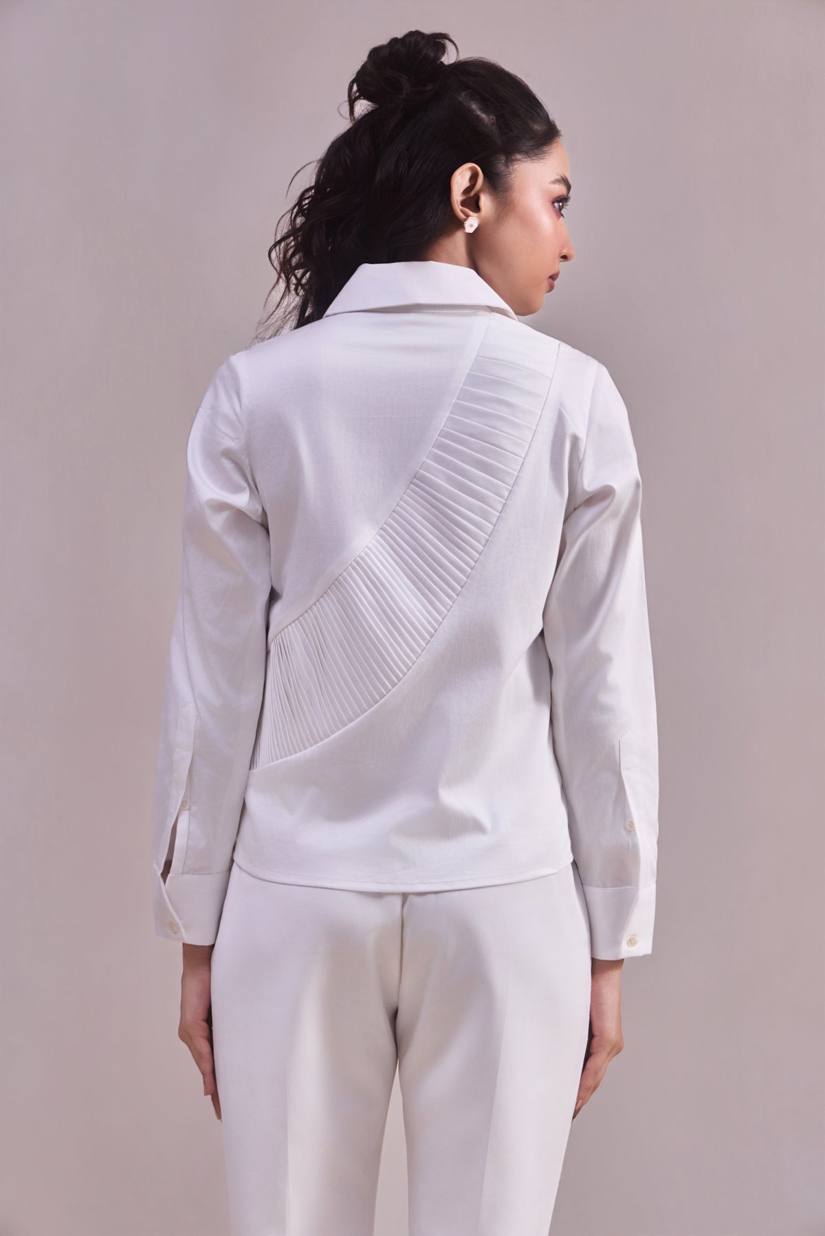 Woman wearing a white jacket with pleated details on a plain background