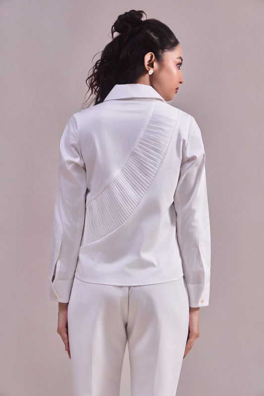 Woman wearing a white jacket with pleated details on a plain background