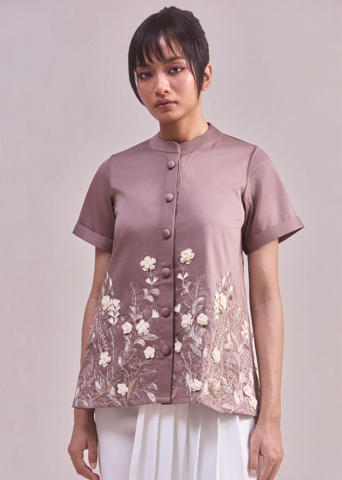 Woman wearing a mauve blouse with floral embroidery on a plain background
