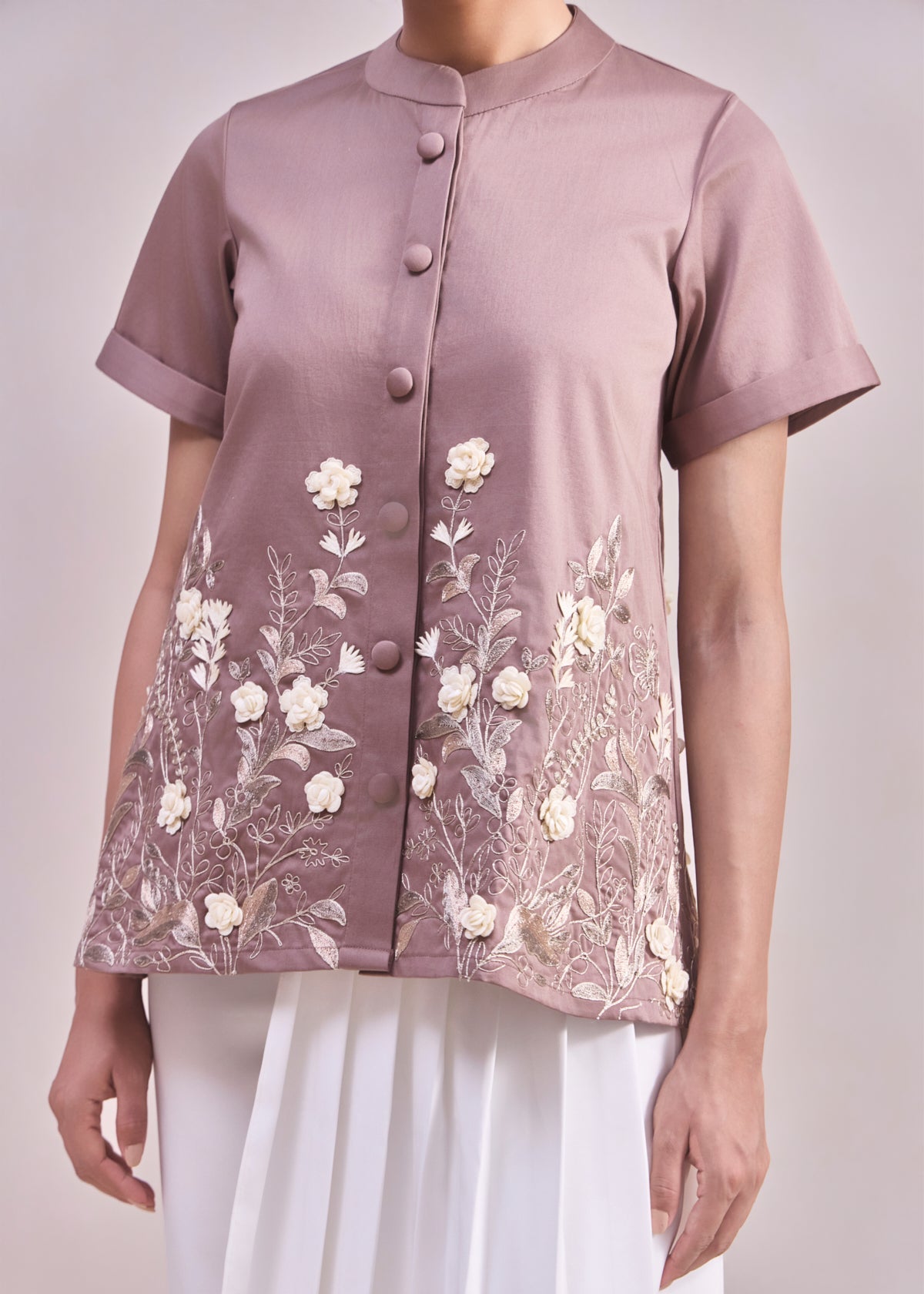 Person wearing a mauve blouse with floral embroidery on a plain background