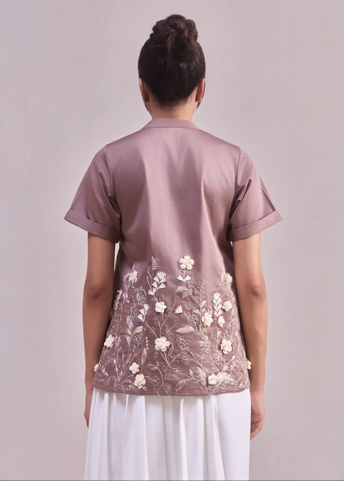 Person wearing a mauve blouse with floral embroidery on a plain background