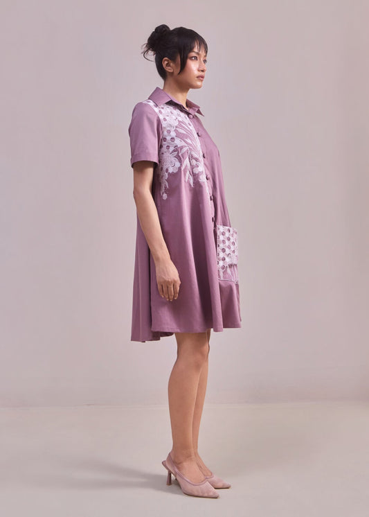 Woman wearing a purple dress with white floral patterns on a plain background
